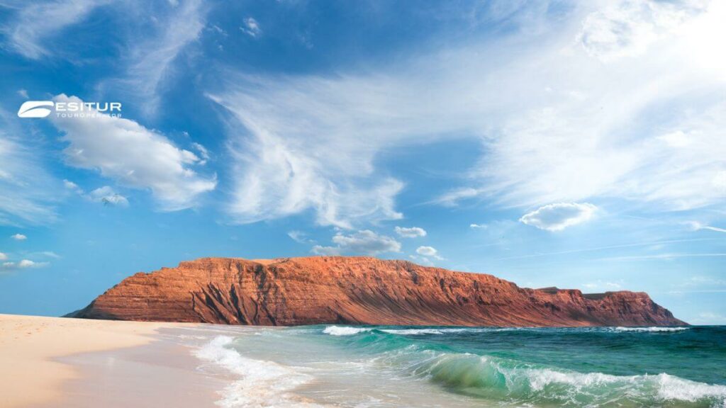 Spiaggia di Lanzarote con mare turchese e scogliera rossa, Quando andare alle Canarie per un viaggio al mare