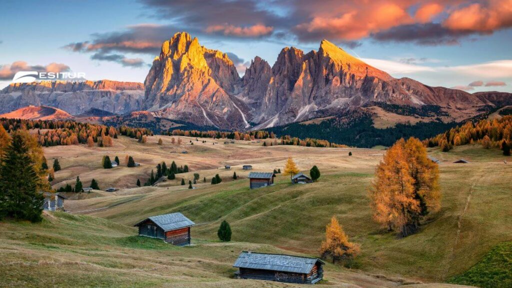 Prati e baite ai piedi delle Dolomiti illuminate al tramonto, foliage in Italia durante un viaggio autunnale
