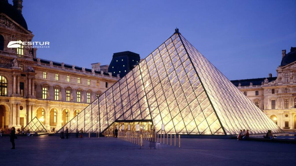 Piramide del Louvre illuminata di sera nel cortile del museo, viaggio a Parigi e Versailles